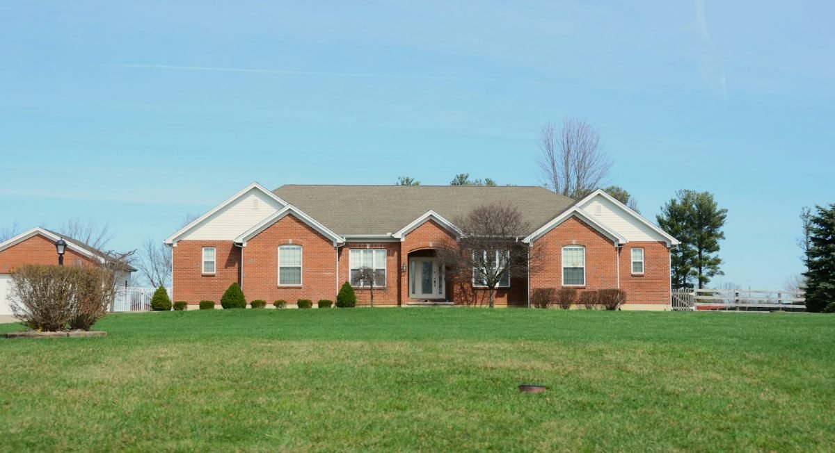 A brick ranch house with a brown shingle roof and a wide lawn