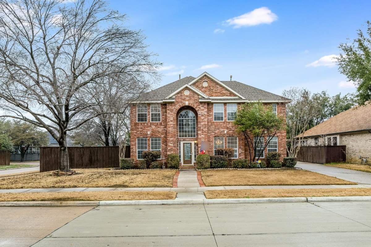 A two-story brick house with a shingle roof and a Texas flag by the door