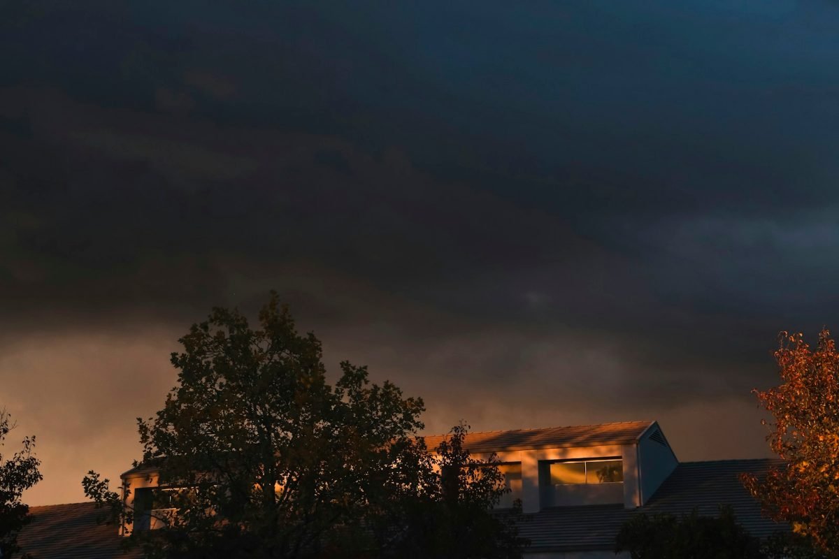 A dark storm sky over trees and rooftops at dusk