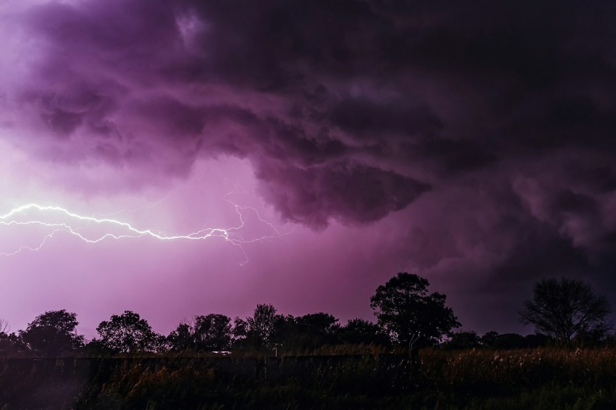 Lightning under purple storm clouds over flat brushland