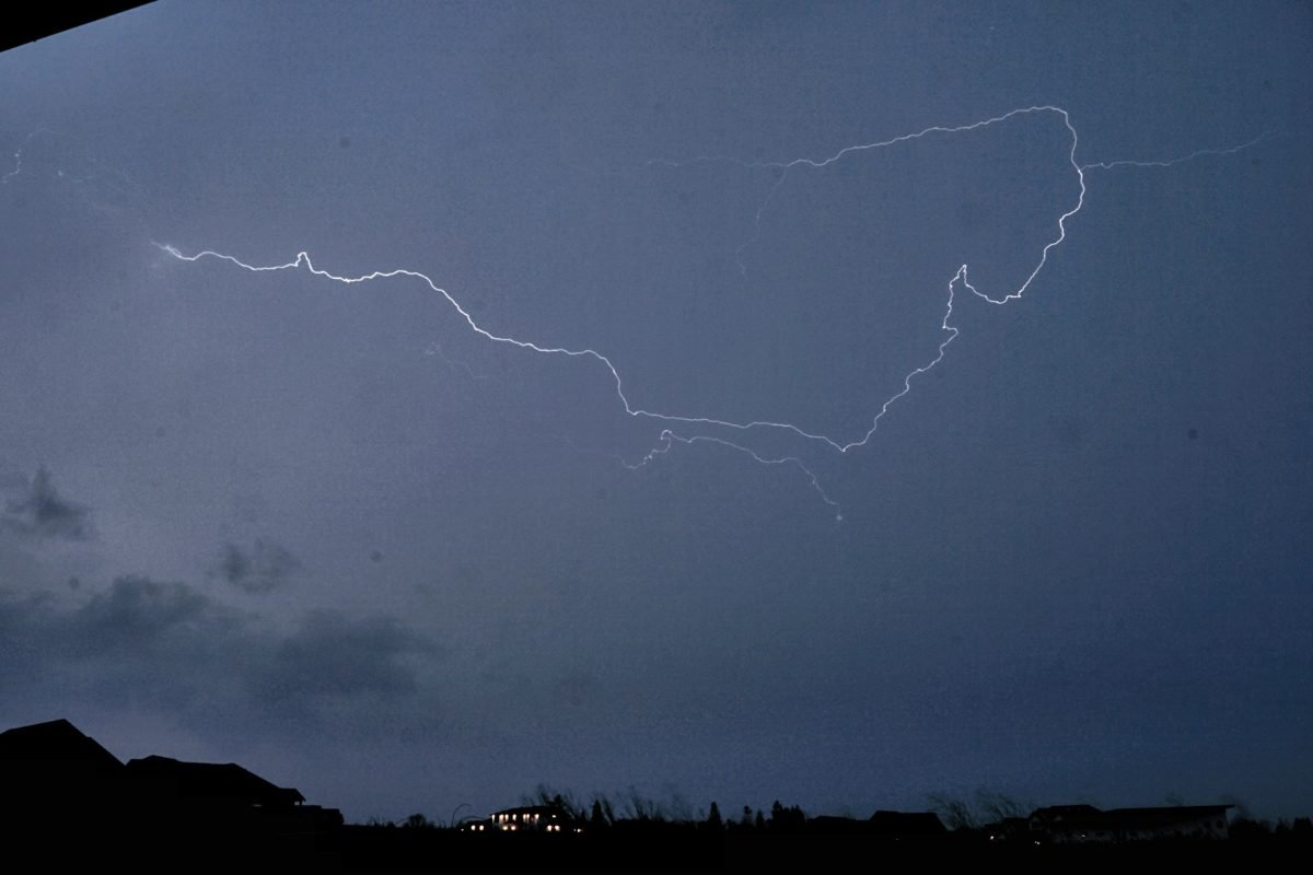 A long lightning bolt across a stormy sky above a town