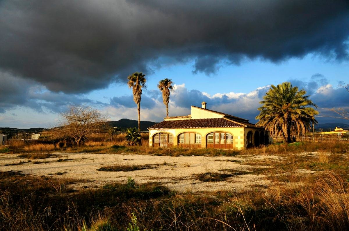 A dark storm cloud over a house, palms and dry open land