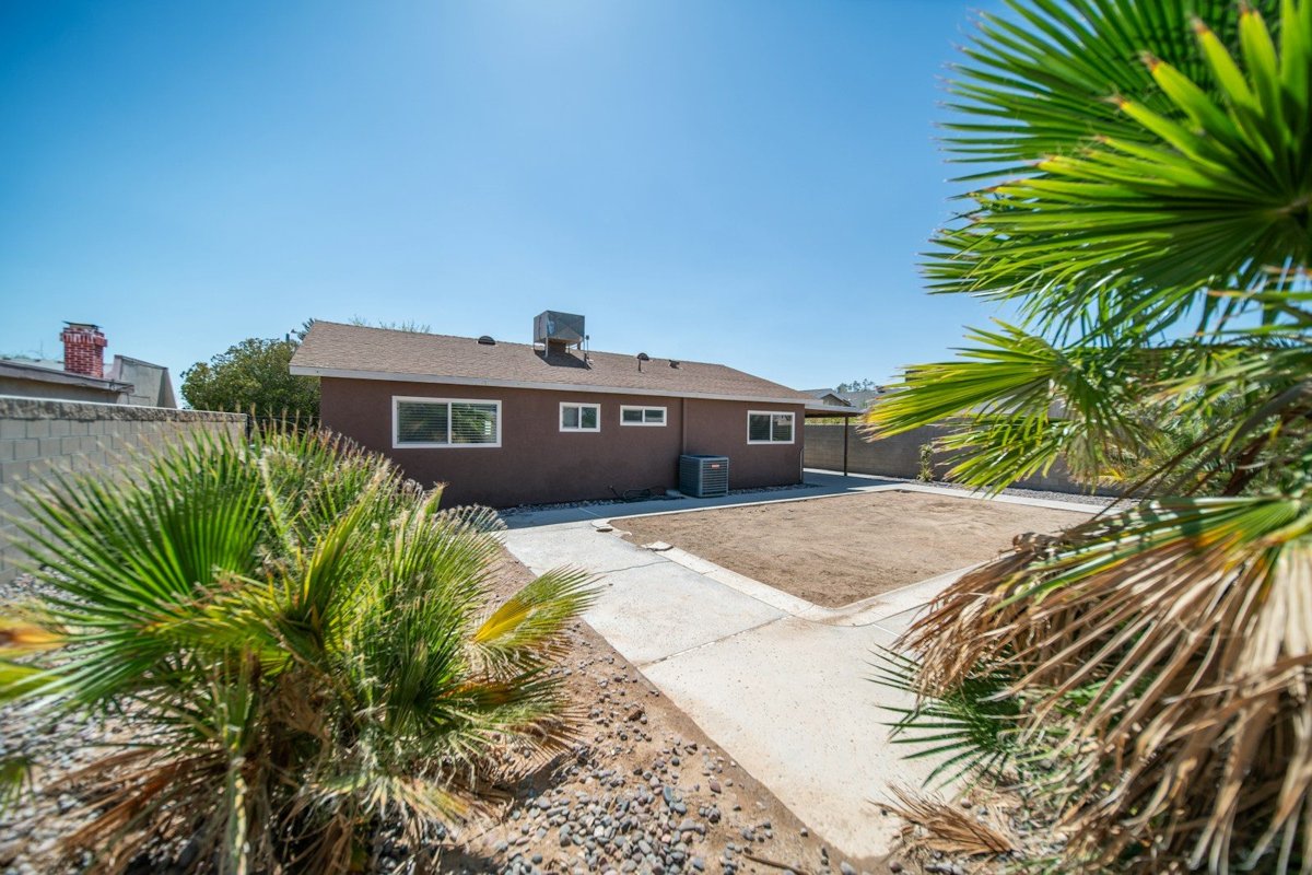 A single-story stucco house with a shingle roof behind fan palms